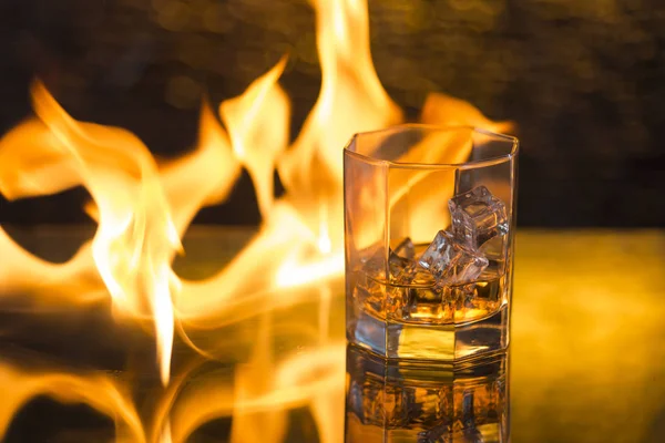 Glass of whisky with ice on a black background and fire flames — Stock Photo, Image