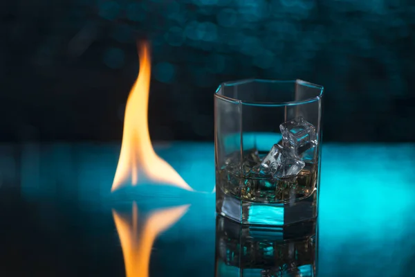 Vaso de whisky con hielo sobre fondo azul y llamas de fuego — Foto de Stock