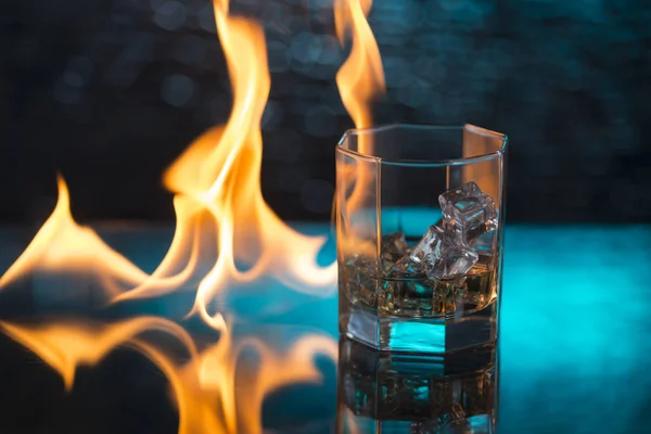 Vaso de whisky con hielo sobre fondo azul y llamas de fuego — Foto de Stock