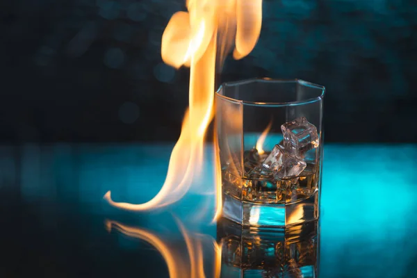 Glass of whisky with ice on a blue background and fire flames — Stock Photo, Image