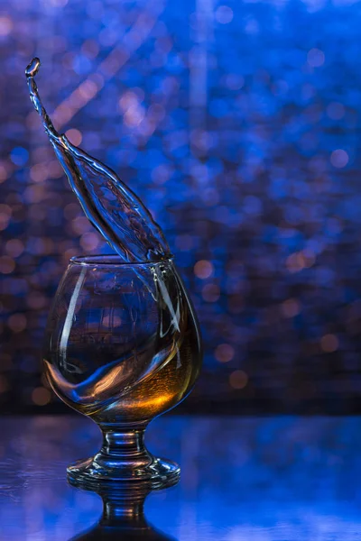 Bicchiere da vino di cognac e spruzzi su uno sfondo blu bokeh — Foto Stock