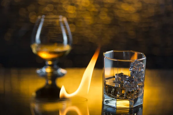 Скляний віскі з льодом і келихом коньяку і полум'я вогню на жовтому фоні боке — стокове фото