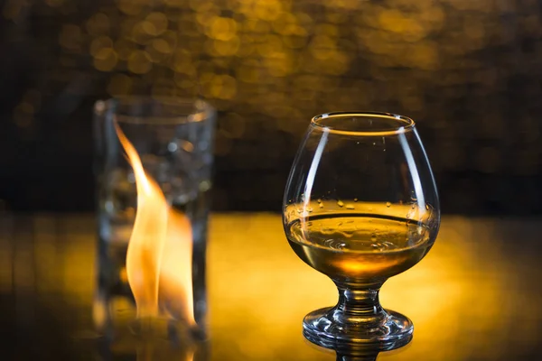 Vaso o whisky con hielo y vino de coñac y llamas de fuego sobre fondo amarillo bokeh — Foto de Stock