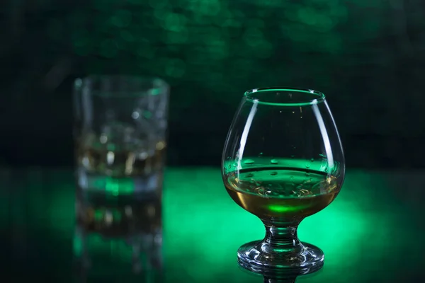 Bicchiere o whisky con ghiaccio e bicchiere da vino di cognac su sfondo verde bokeh — Foto Stock