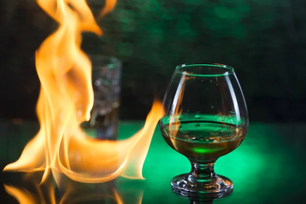 Bicchiere o whisky con ghiaccio e bicchiere da vino di cognac e fiamme di fuoco su sfondo verde bokeh — Foto Stock