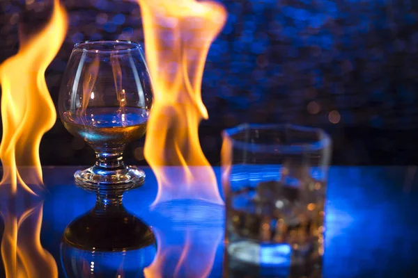 Bicchiere o whisky con ghiaccio e bicchiere da vino di cognac e fiamme di fuoco su sfondo bokeh — Foto Stock