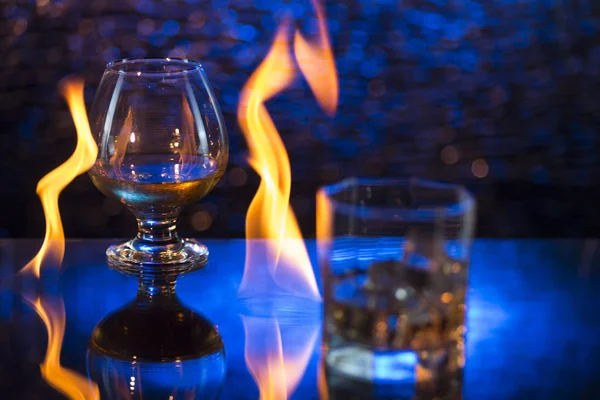 Bicchiere o whisky con ghiaccio e bicchiere da vino di cognac e fiamme di fuoco su sfondo bokeh — Foto Stock