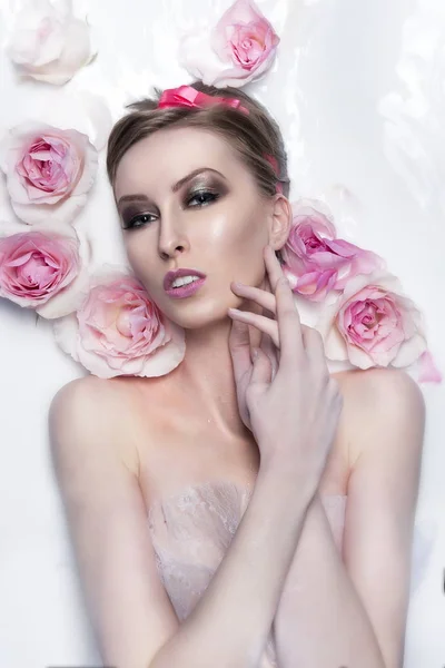 Retrato da menina na banheira de hidromassagem cheia de leite com flores de rosas — Fotografia de Stock