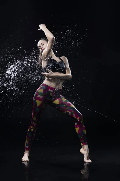 The girl dances on the floor covered with water on a black backg