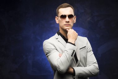 adam gri bir takım ve mavi bir arka plan üzerinde güneş gözlüğü.