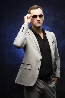 adam gri bir takım ve mavi bir arka plan üzerinde güneş gözlüğü.