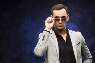 adam gri bir takım ve mavi bir arka plan üzerinde güneş gözlüğü.