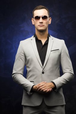 adam gri bir takım ve mavi bir arka plan üzerinde güneş gözlüğü.