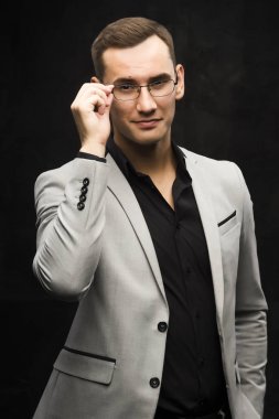 Gri bir takım ve karanlık bir arka plan üzerinde gözlük genç adam.