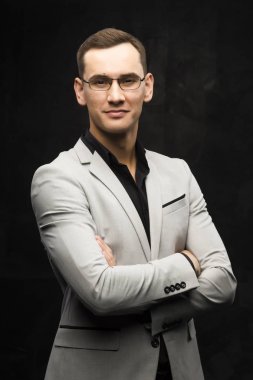 Gri bir takım ve karanlık bir arka plan üzerinde gözlük genç adam.