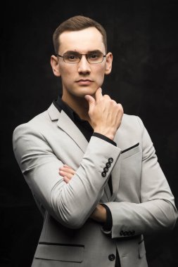 Gri bir takım ve karanlık bir arka plan üzerinde gözlük genç adam.