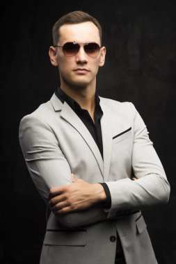 Genç adam gri bir takım ve karanlık bir arka plan üzerinde güneş gözlüğü