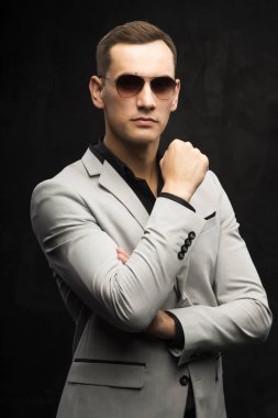 Genç adam gri bir takım ve karanlık bir arka plan üzerinde güneş gözlüğü
