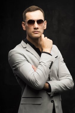 Genç adam gri bir takım ve karanlık bir arka plan üzerinde güneş gözlüğü