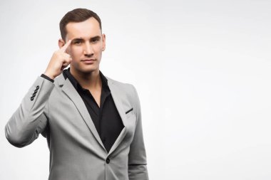 Gri takım elbise giyen genç bir adam başına bir işaret parmağını gösterir.