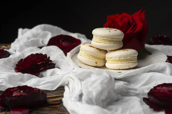 Τρεις macaroons ζαχαροπλαστικής ξαπλωμένη σε ένα πιάτο που περιβάλλεται από τριαντάφυλλο bloss — Φωτογραφία Αρχείου