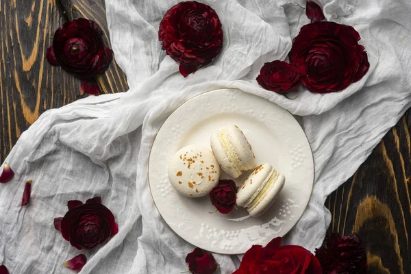 Three macaroons pastry lying on a plate surrounded by rose bloss