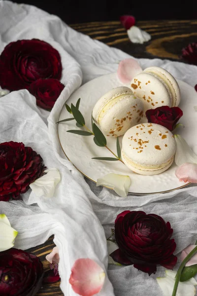 Three macaroons pastry lying on a plate surrounded by rose bloss