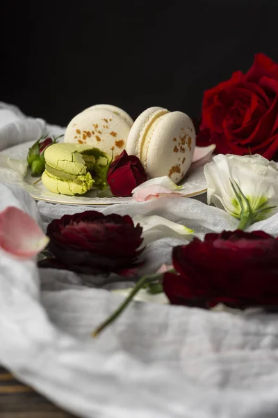 Τρεις macaroons ζαχαροπλαστικής ξαπλωμένη σε ένα πιάτο που περιβάλλεται από τριαντάφυλλο bloss — Φωτογραφία Αρχείου