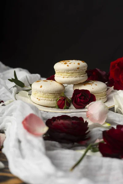 Τρεις macaroons ζαχαροπλαστικής ξαπλωμένη σε ένα πιάτο που περιβάλλεται από τριαντάφυλλο bloss — Φωτογραφία Αρχείου