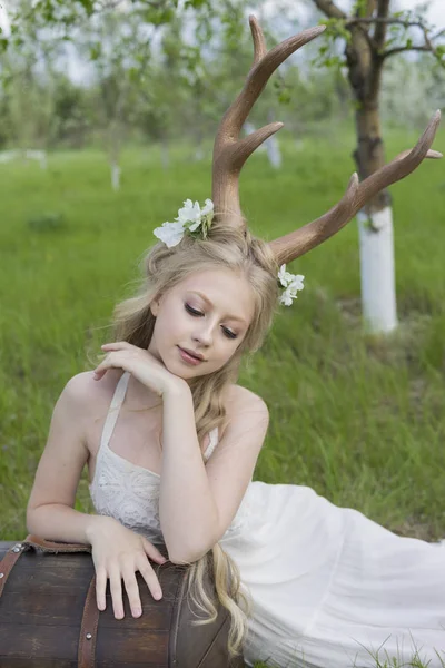 Menina loira adolescente vestindo vestido branco com chifres de veado em sua cabeça — Fotografia de Stock