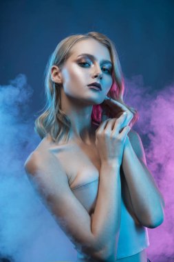 Güzel sarışın ve makyajlı genç bir kız yüzüne dokunuyor. 