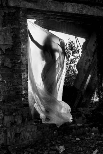 Slender nude girl, covered by a cellophane film, through which only her silhouette is visible and her nakedness is covered, in the ruins of a destroyed building. Conceptual, artistic, creative design