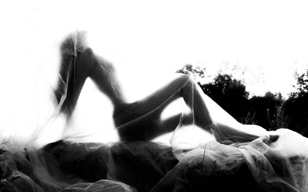 Slender nude girl, covered by a cellophane film, through which only her silhouette is visible and her nakedness is covered, in the ruins of a destroyed building. Conceptual, artistic, creative design