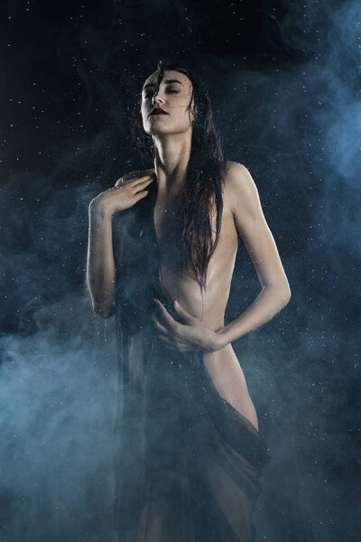 Beautiful slim wet nude girl, posing in the rain, theatrical fog