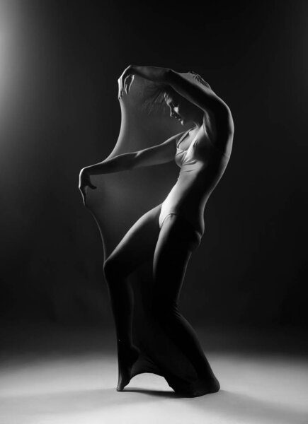 Slim girl wearing a white bodysuit dances a modern avant garde dance, covering her body with elastic transparent fabric. Artistic, conceptual, monochrome and creative design. Silhouette photography