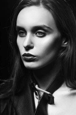 Kırmızı dudaklı, düğmesiz bir ceket giyen ve boynuna deri bir kemer takan sarışın bir kız. Elleriyle onu çekiyor, arka planda, bir lambanın yanında. Tek renkli tasarım