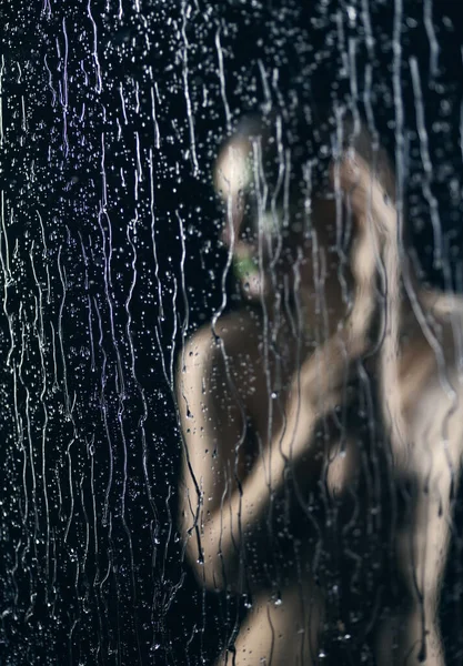 一个漂亮的裸体女孩 穿着脱光了眼睛的衣服 在窗玻璃后面摆姿势 窗玻璃上的溪流和雨滴在黑色的背景上流下来 艺术性模糊设计 — 图库照片