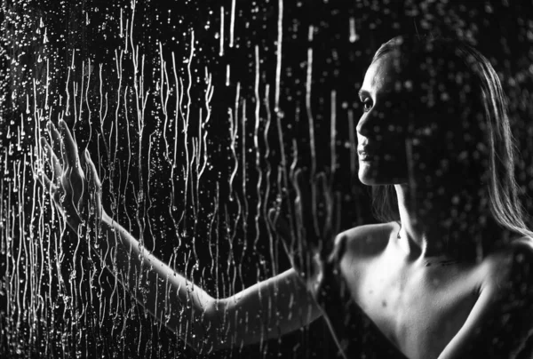 一个美丽的裸体女孩用双手触摸着一个玻璃窗 玻璃窗上的溪流和雨滴在黑色的背景上流下来 艺术单色设计 — 图库照片