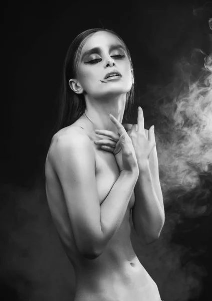 一个漂亮的身材苗条 赤身裸体 头戴前卫妆容的女孩 双手捂住胸部 在黑色的背景下冒着浓烟 广告单色设计 — 图库照片