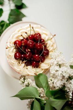 Kırmızı böğürtlen pastası, kiraz çileği ve beyaz kremayla süslenmiş, leylak çiçekleri ve yeşil yaprakların arasında. Yemek fotoğrafçılığı. Reklam ve ticari tasarım
