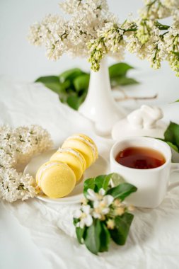 Beyaz leylak çiçekleri ve yeşil yaprakların arasında sarı badem kurabiyeleri. Yemek fotoğrafçılığı. Reklamcılık ve ticari yakın plan tasarımı