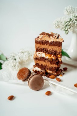 Cam bir tabakta çeşitli kurabiye ve fındıkla süslenmiş çikolatalı pasta ve leylak ve yeşil yapraklardan oluşan beyaz çiçekler arasında badem kurabiyesi. Yemek fotoğrafçılığı. Reklamcılık ve ticari yakın plan tasarımı