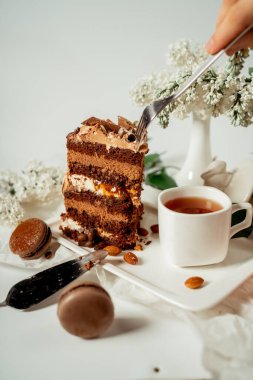 Cam bir tabakta çeşitli kurabiye ve fındıkla süslenmiş çikolatalı pasta ve leylak ve yeşil yapraklardan oluşan beyaz çiçekler arasında badem kurabiyesi. Yemek fotoğrafçılığı. Reklamcılık ve ticari yakın plan tasarımı