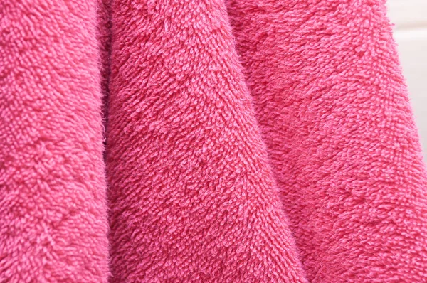 Wavy dry bath towels of color pink hanging in bathroom close-up