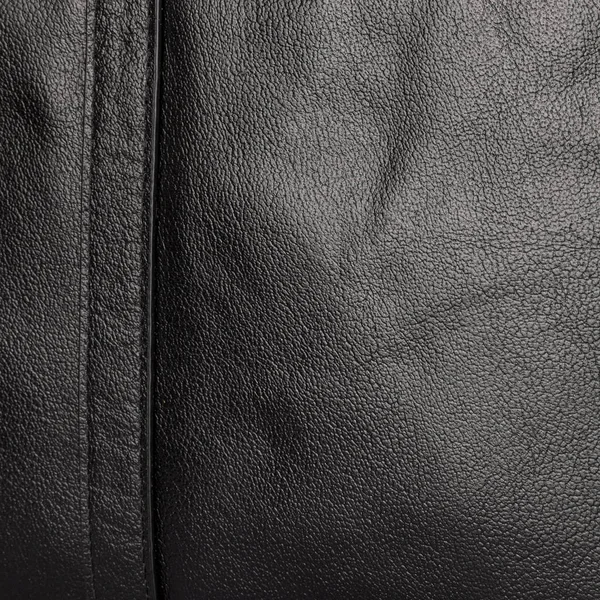 The texture of the two stitched halves of soft black leather with a neat stitch