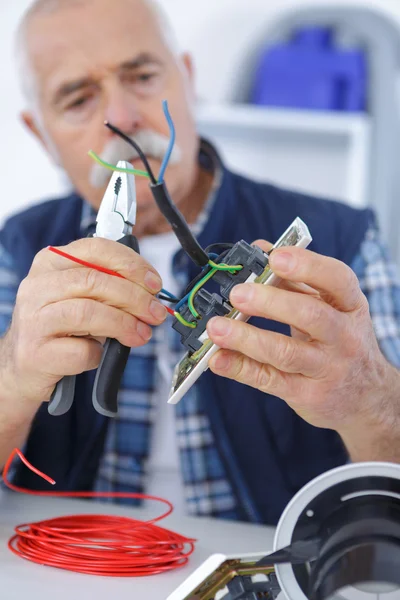 Senior electrician is fixing an outlet with pliers — Stock Photo, Image