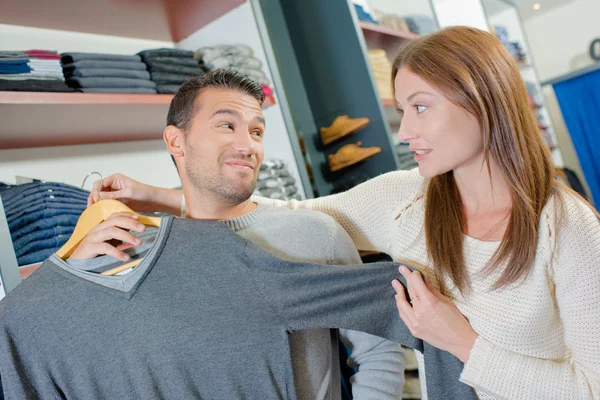 Пара в магазині одягу, леді тримає светр проти чоловіка — стокове фото
