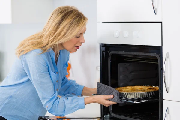 Bonita mujer rubia poniendo tarta en el horno para hornear —  Fotos de Stock