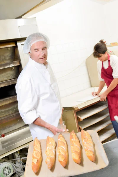 Baker looking at French sticks — Stock Photo, Image