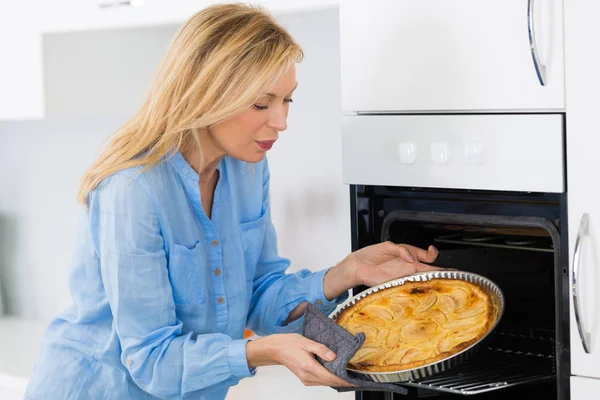 Mujer rubia madura hornear tarta en el horno —  Fotos de Stock